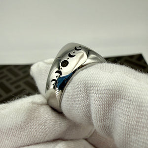 A polished silver ring with engraved crescent moon and star motifs, resting on a white textured fabric sleeve.