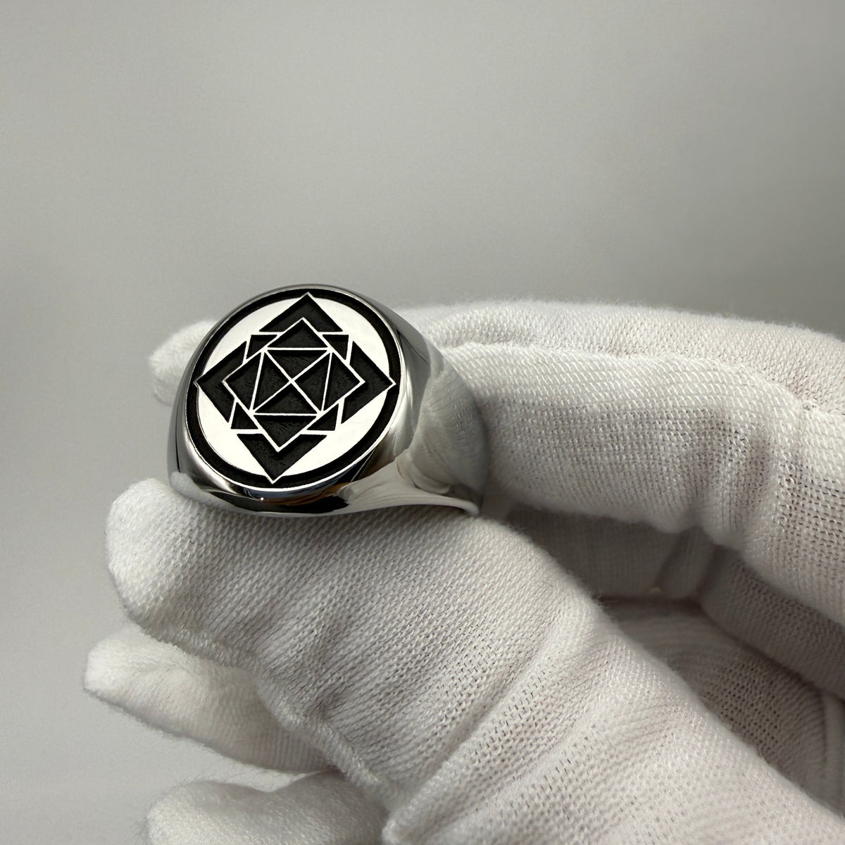 Round stainless steel signet ring with a geometric engraved design and black background