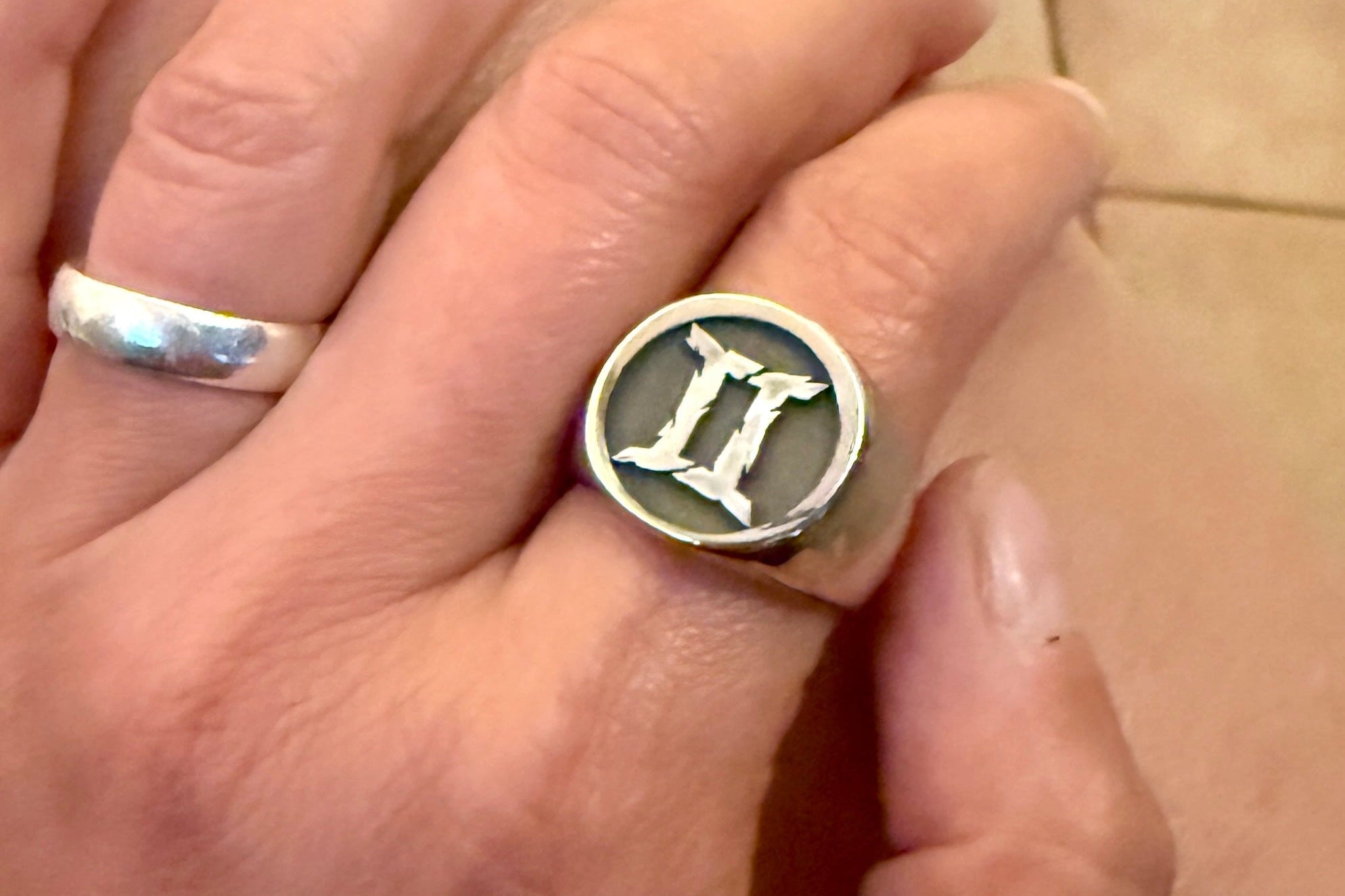 Hand wearing a stainless steel signet ring with a zodiac symbol on a tiled floor background