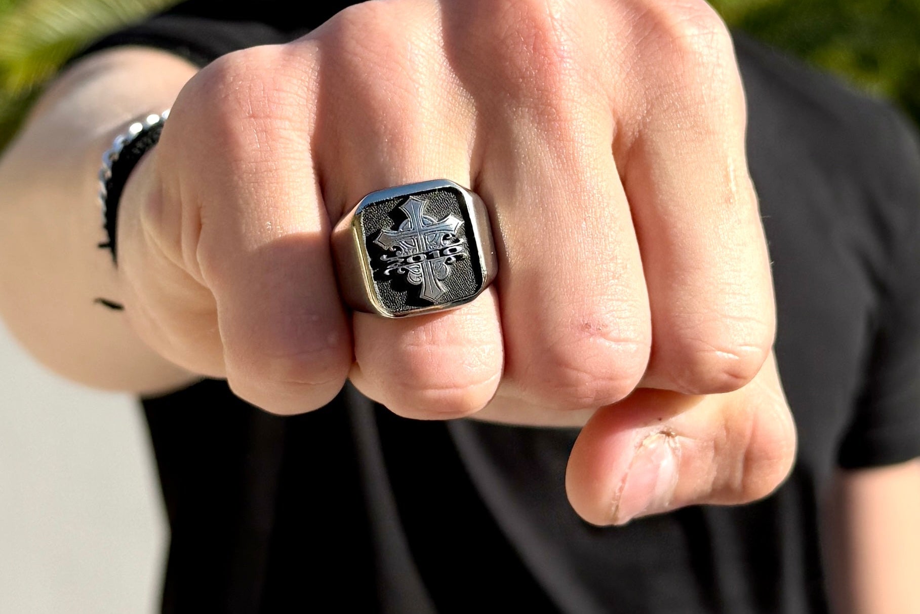 Person wearing a stainless steel signet ring with a detailed design outdoors