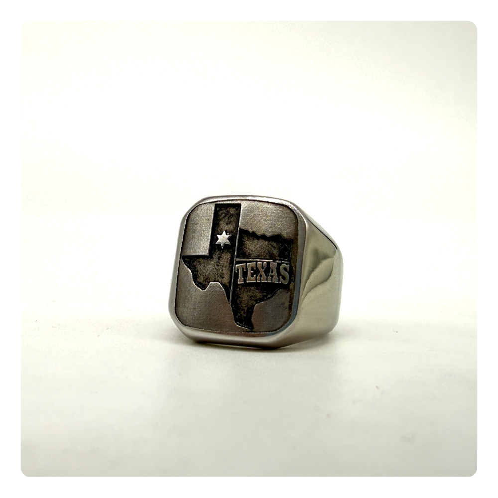 A silver-toned signet ring featuring an engraved map of Texas with the word 'TEXAS' and a star, displayed on a light neutral background.