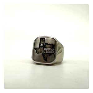A silver-toned signet ring featuring an engraved map of Texas with the word 'TEXAS' and a star, displayed on a light neutral background.
