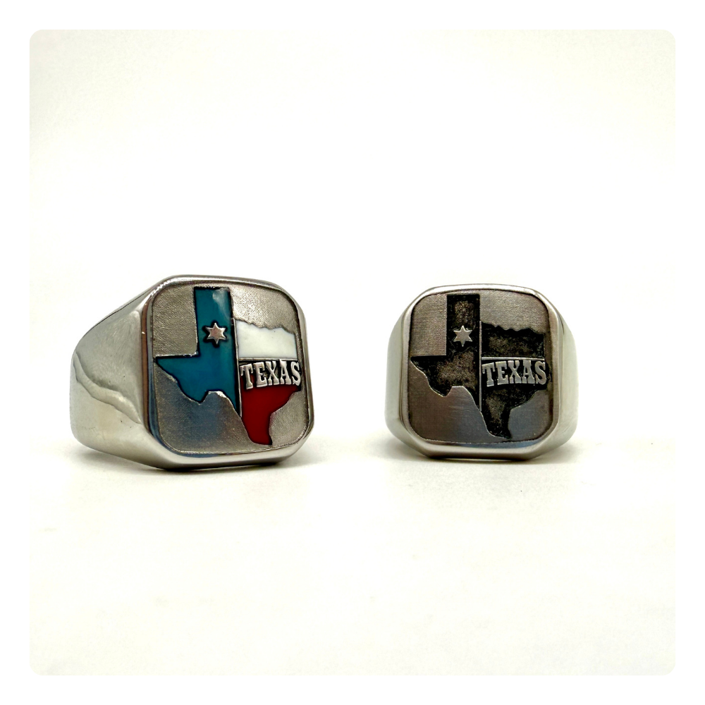 A pair of silver-toned signet rings featuring the state of Texas, one with a blue and red Texas flag design and the other with a distressed black and silver Texas flag design, set against a plain white background.